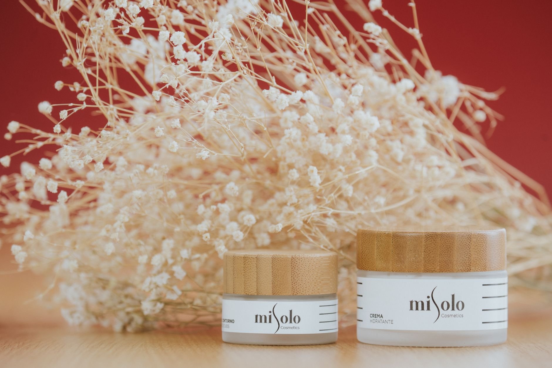 Two elegant skincare cream jars with refined packaging amidst dried white flowers on a warm background