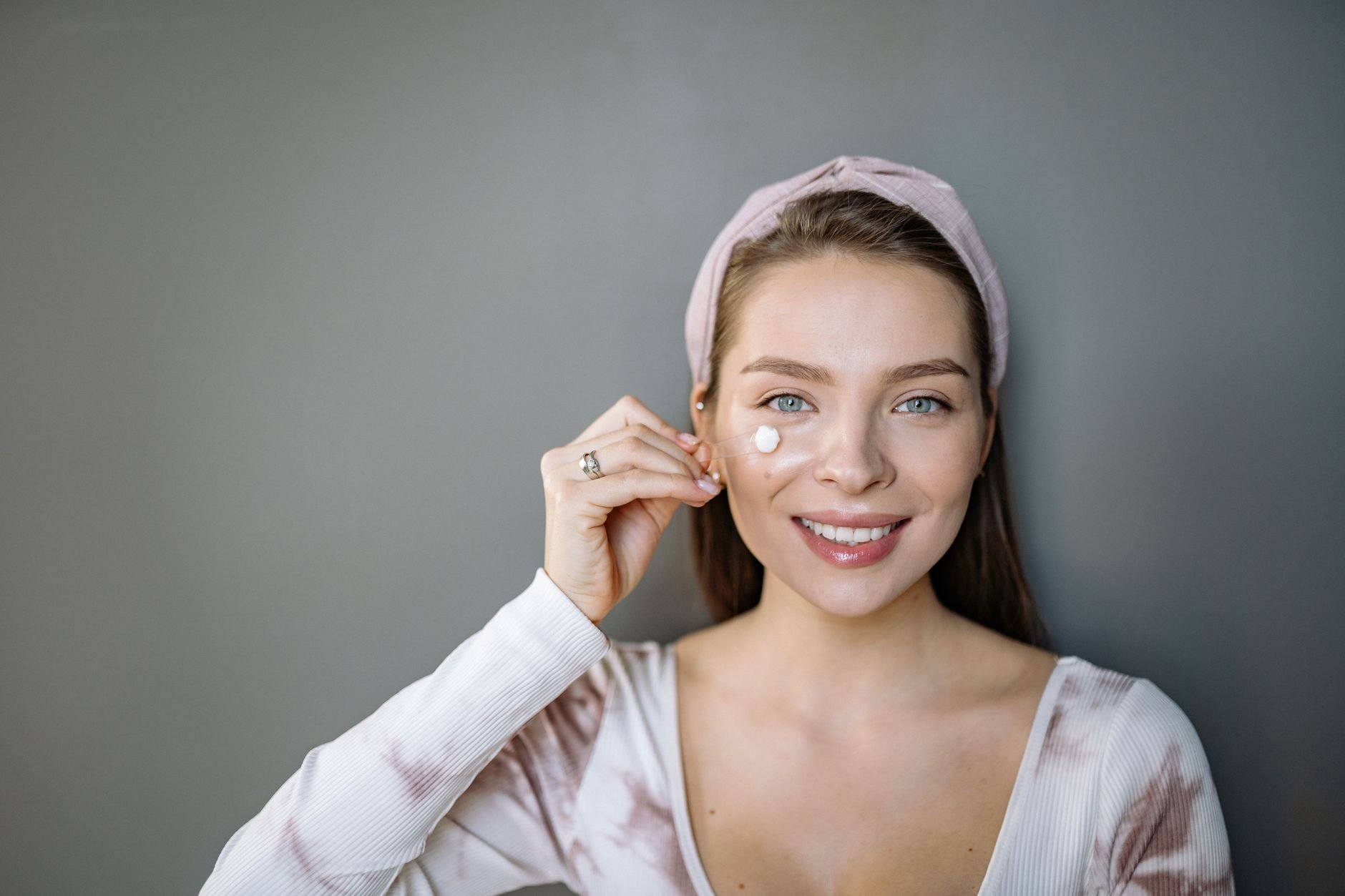 A woman with luminous skin applying luxury skincare, smiling softly